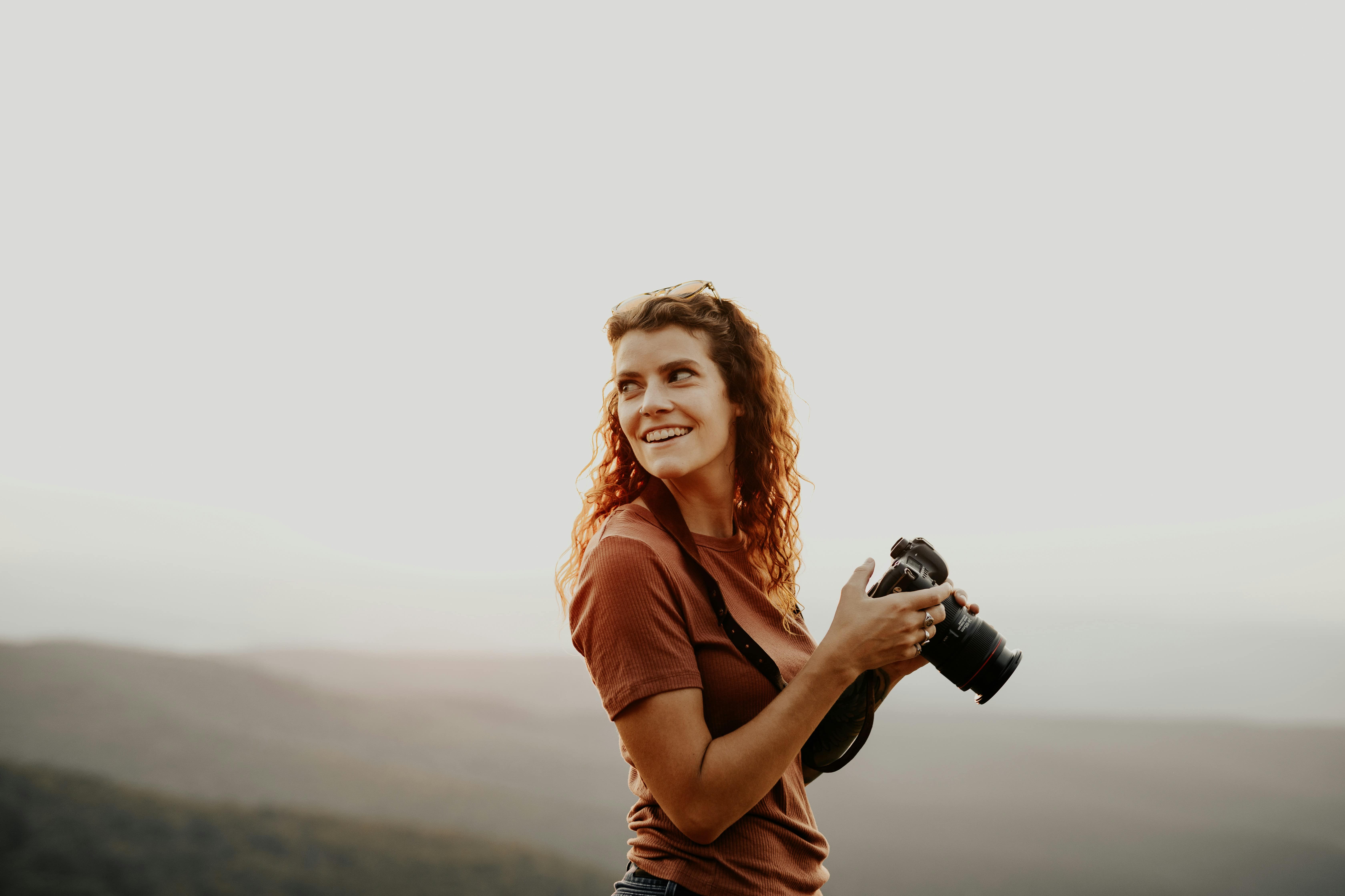 Une femme rousse tenant un appareil photo en souriant
